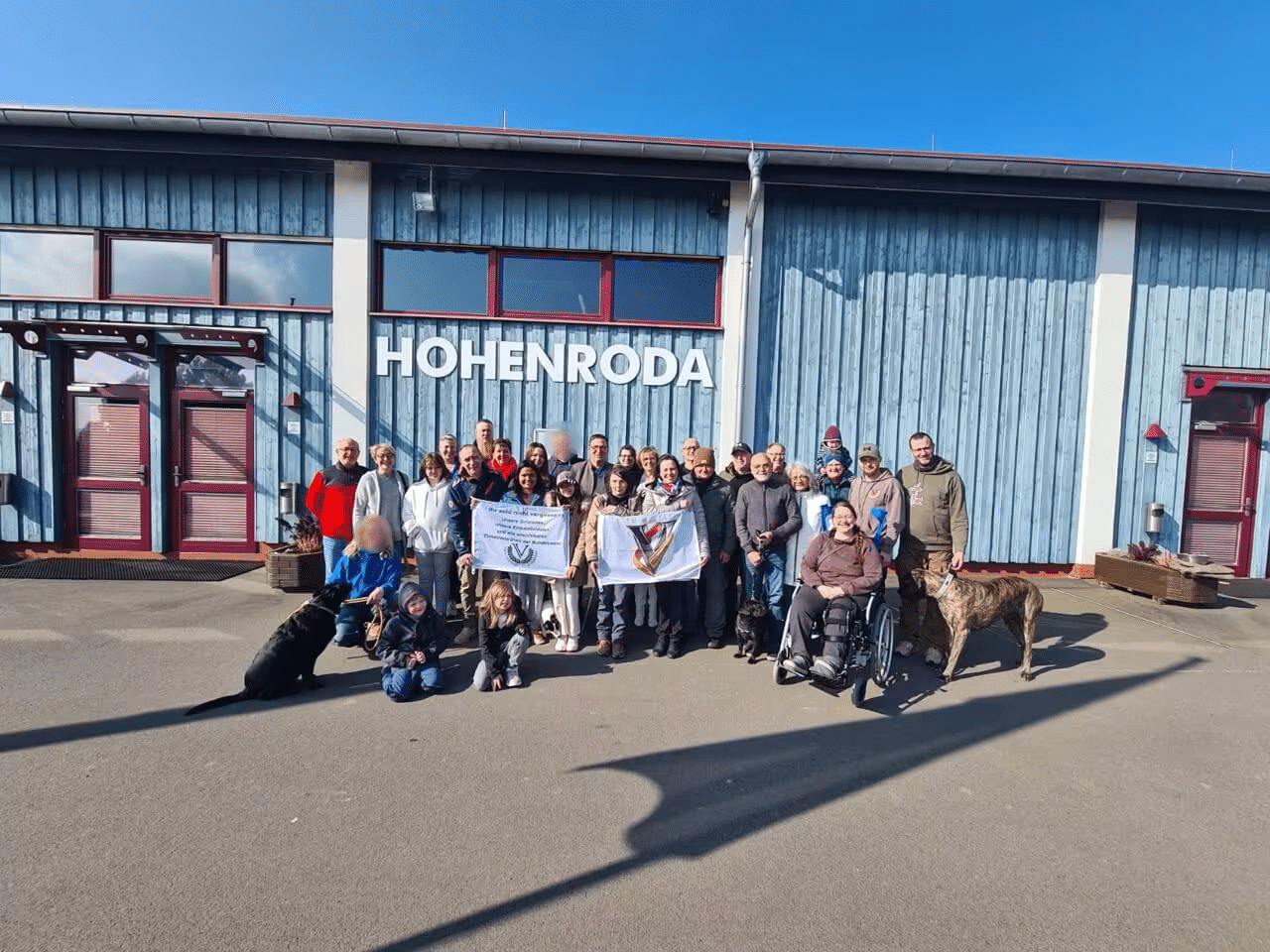 Neues Gruppenbild Gruppenfoto vom Bund Deutscher Veteranen mit Hunden vor dem blauen Gebäude "HOHENRODA" bei sonnigem Wetter.